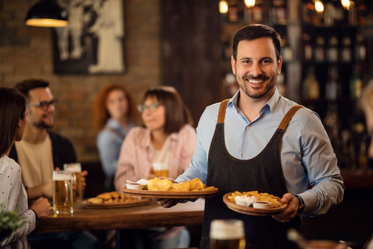 Garçom sorridente segurando bandejas de aperitivos em restaurante